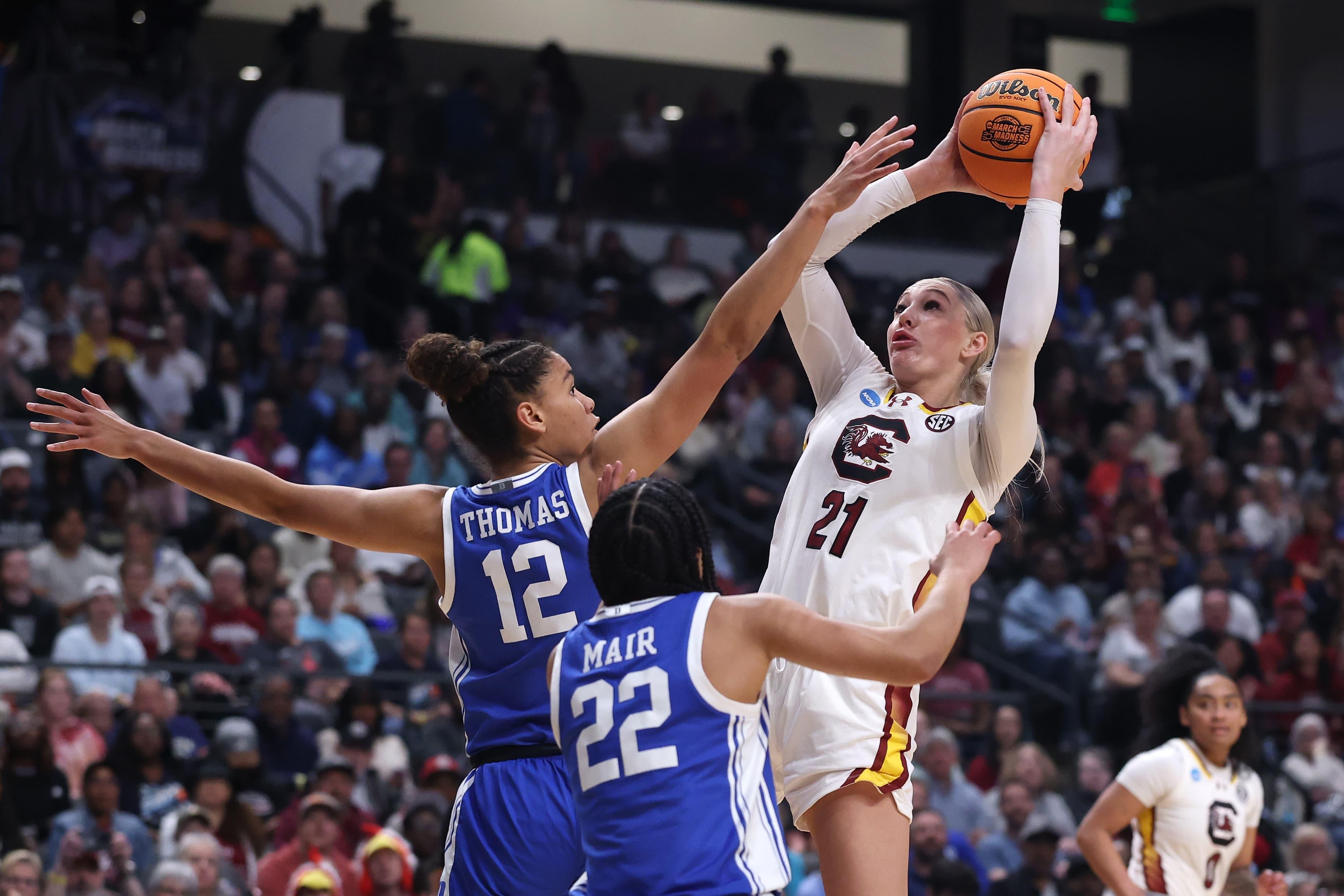 A women's basketball player goes up for a rebound over a defender.